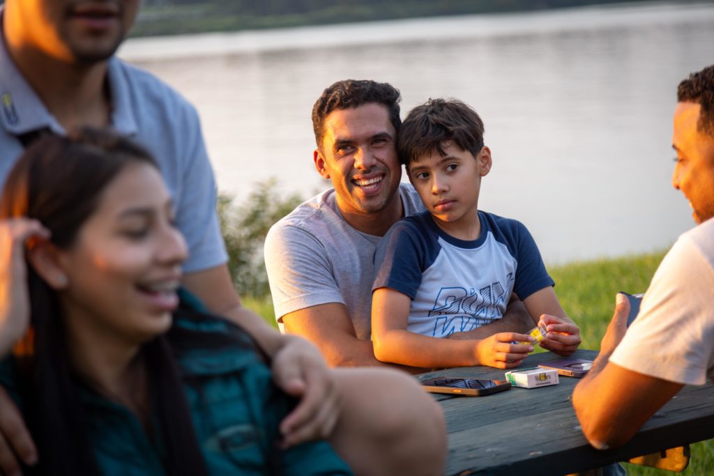A group enjoys an outdoor gathering near a body of water during what appears to be a warm, sunny day.