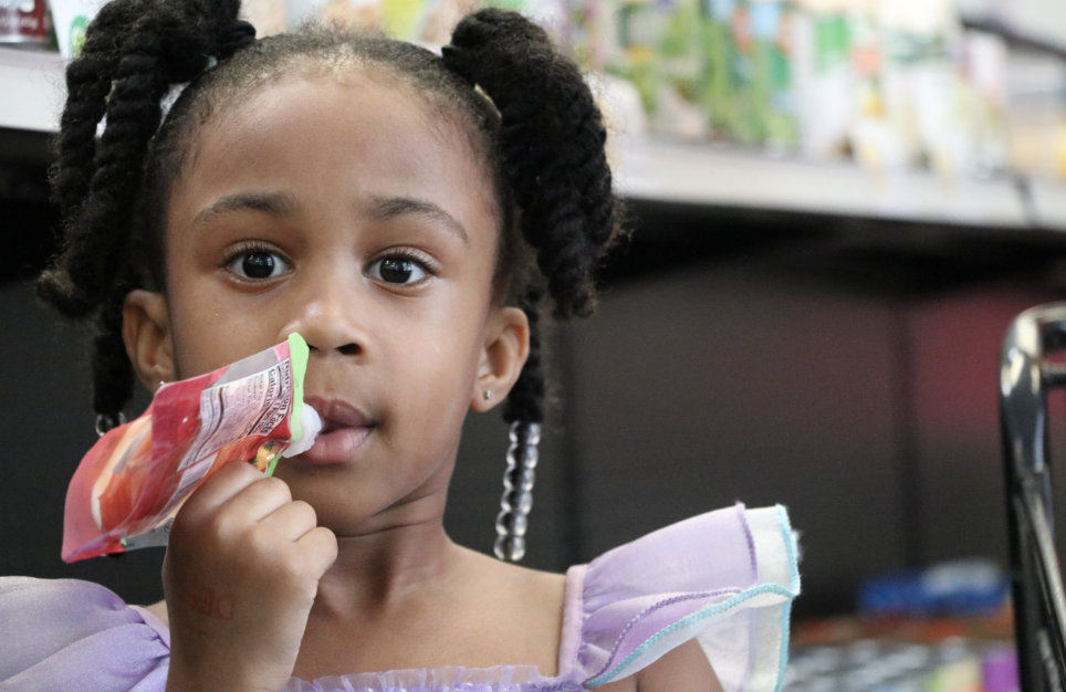 A child in a purple sleeve costume is focused on eating a colorful frozen treat.