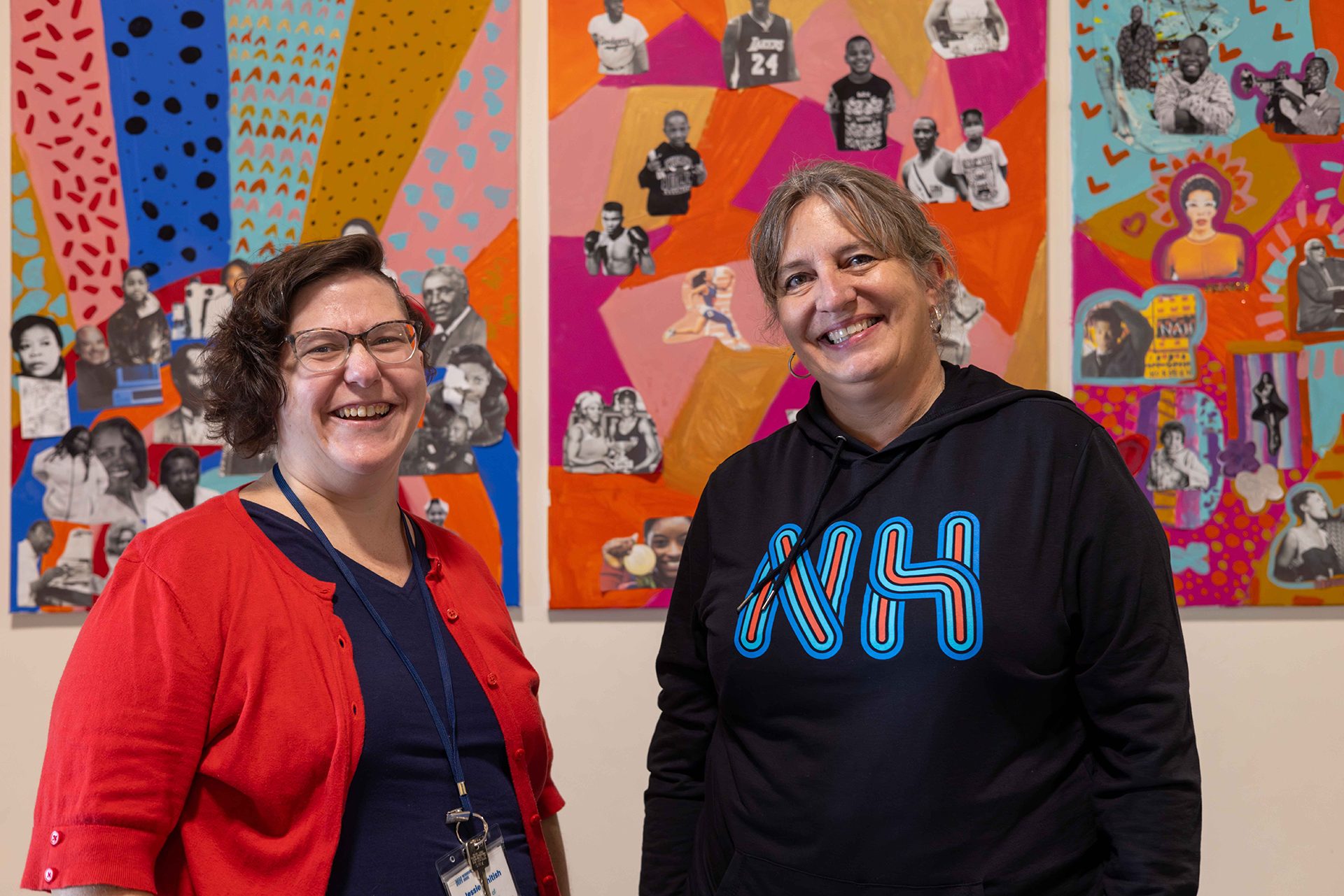 Two individuals are smiling and posing in front of a colorful, abstract background with various stylized figures.